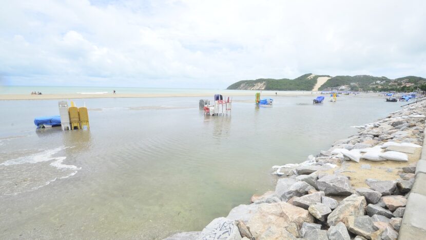 Poça extensa de água da chuva sobre a faixa de areia da praia, com o Morro do Careca ao fundo