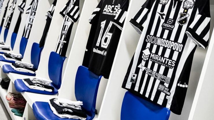 Camisas alvinegras do ABC penduradas lado a lado, acima de assentos azuis