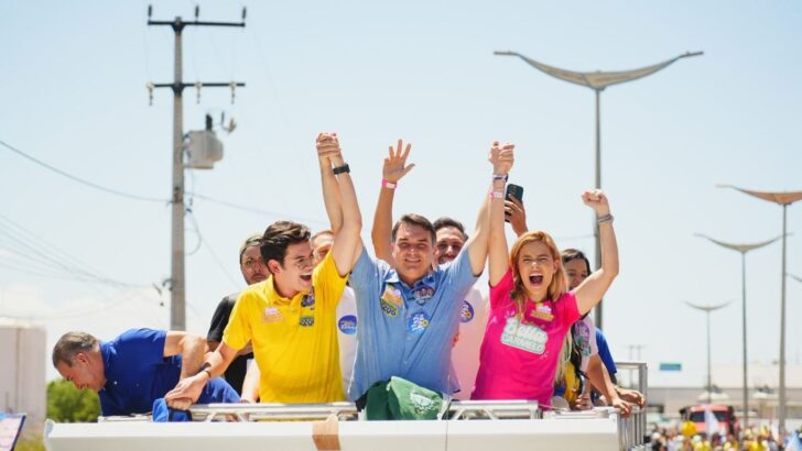 Grupo de pessoas com camisetas coloridas ergue os braços em cima de um carro de som, diante de multidão