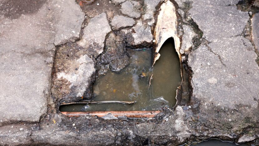 Buraco no calçamento com cano rompido e água de esgoto acumulada