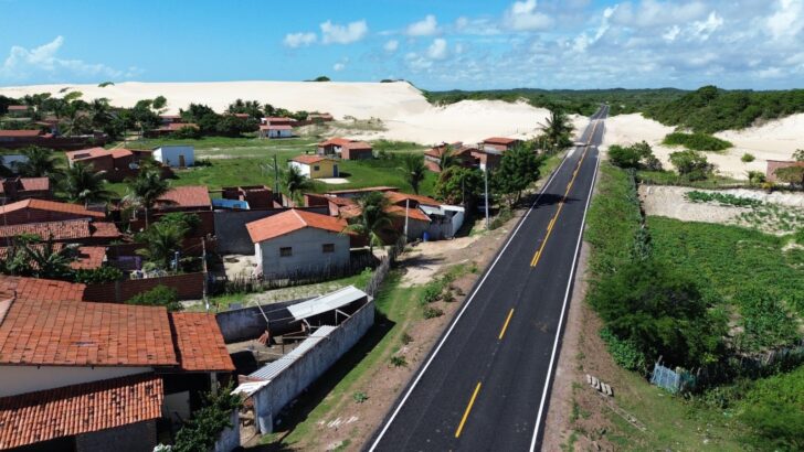 Vista aérea de estrada recém-asfaltada que passa ao lado de casas e dunas