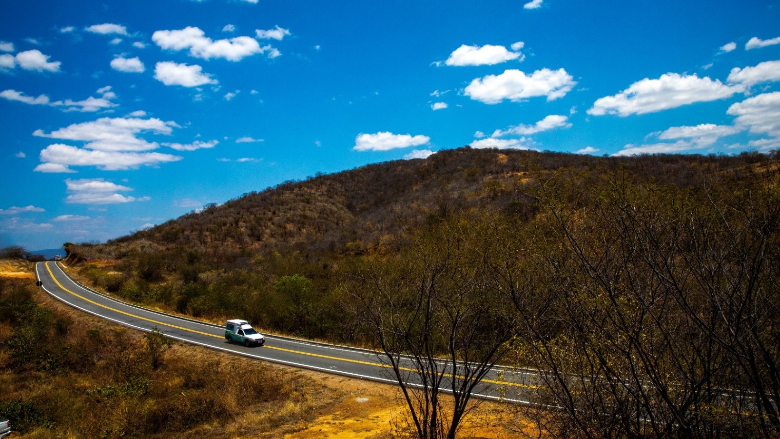 Estrada asfaltada contorna morro com vegetação de caatinga sob céu azul