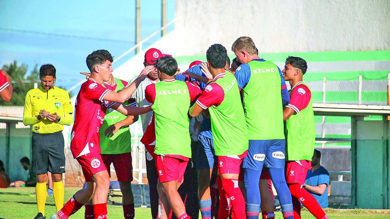 Jogadores de vermelho e reservas de colete verde se abraçam em comemoração