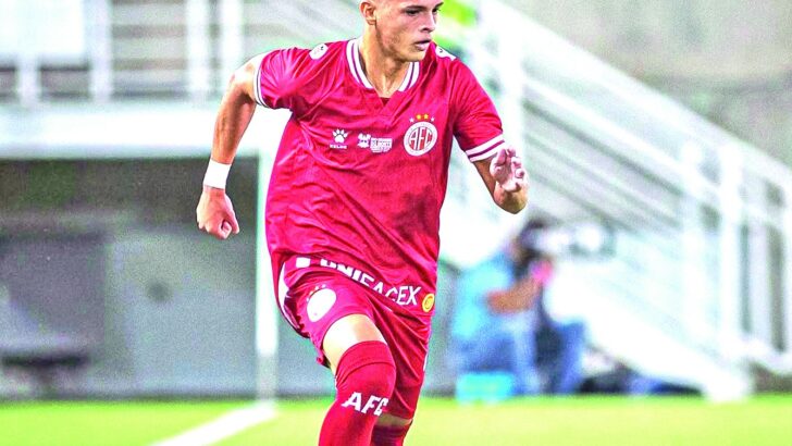 Jogador de camisa vermelha do América conduz a bola em campo