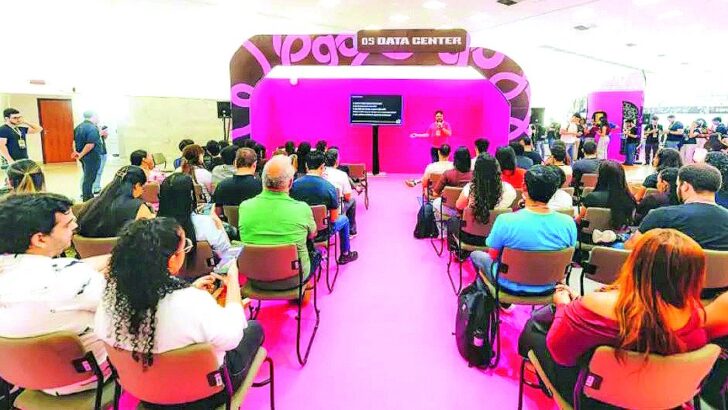 Plateia sentada assiste a palestra em espaço iluminado em rosa no Centro de Convenções