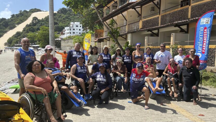 Grupo de pessoas com deficiência e voluntários posa na areia de Ponta Negra