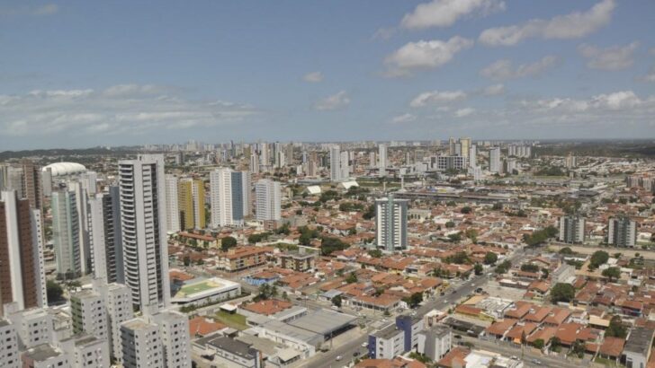 Vista aérea de bairro de Natal com prédios altos, casas de telhado vermelho e céu com nuvens