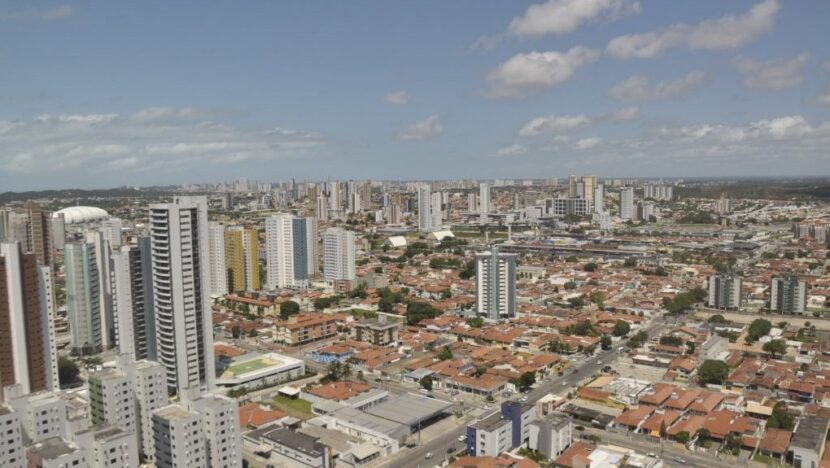 Vista aérea de bairro de Natal com prédios altos, casas de telhado vermelho e céu com nuvens