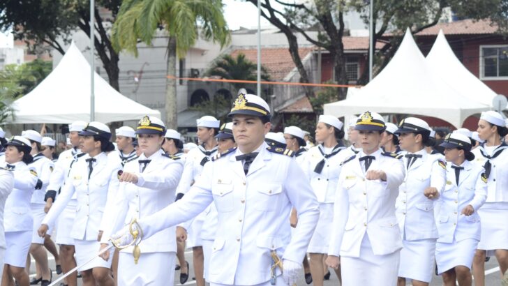 Mulheres de uniforme branco da Marinha marcham em desfile, à frente uma oficial com espada