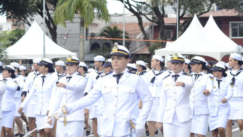 Mulheres de uniforme branco da Marinha marcham em desfile, à frente uma oficial com espada