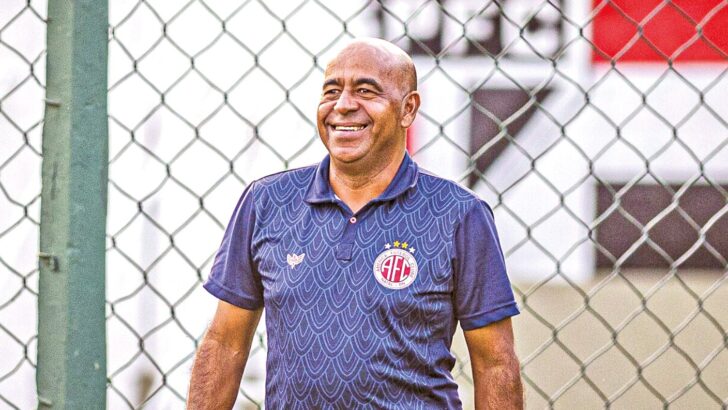 Homem sorridente de camisa azul do América caminha em frente a alambrado