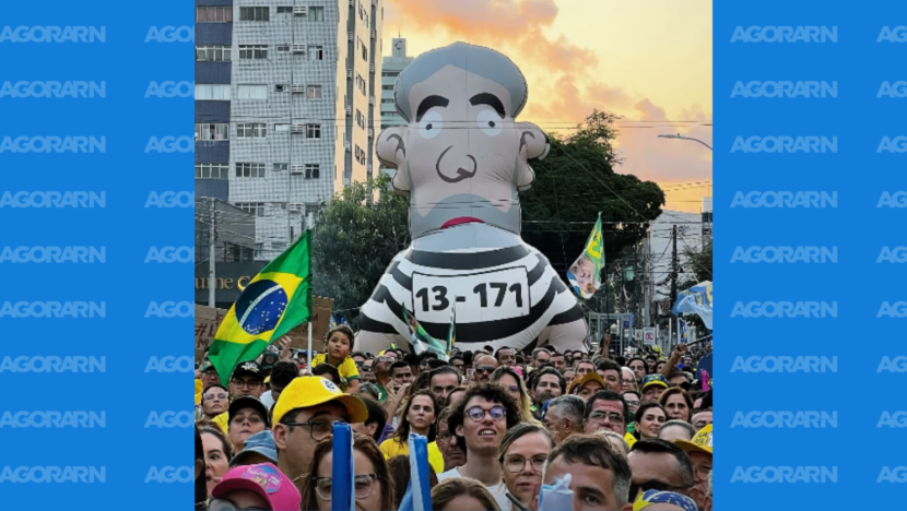 Boneco inflável de Lula com roupa listrada e inscrição “13-171” aparece acima de manifestantes com bandeiras do Brasil no Largo do Atheneu, em Natal.