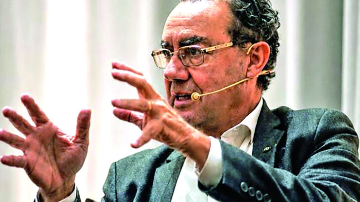 Augusto Cury, sentado e com microfone de lapela, gesticula durante palestra