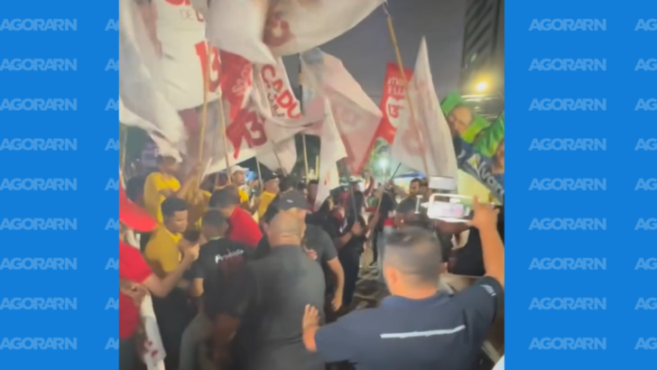 Pessoas com bandeiras do PT e do Brasil se aglomeram à noite diante da TV Ponta Negra, enquanto outras registram a cena com celulares