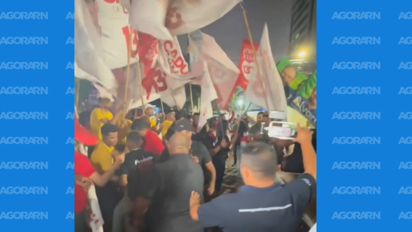 Pessoas com bandeiras do PT e do Brasil se aglomeram à noite diante da TV Ponta Negra, enquanto outras registram a cena com celulares