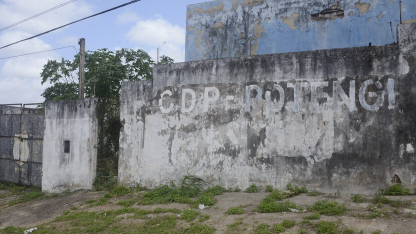 Muro de concreto desgastado com a inscrição CDP - Potengi em letras brancas, portão de ferro fechado à esquerda e mato crescendo na calçada