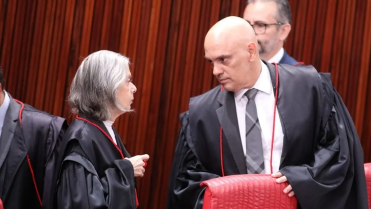 Cármen Lúcia e Alexandre de Moraes conversam, com outro homem ao fundo e um painel de madeira atrás.