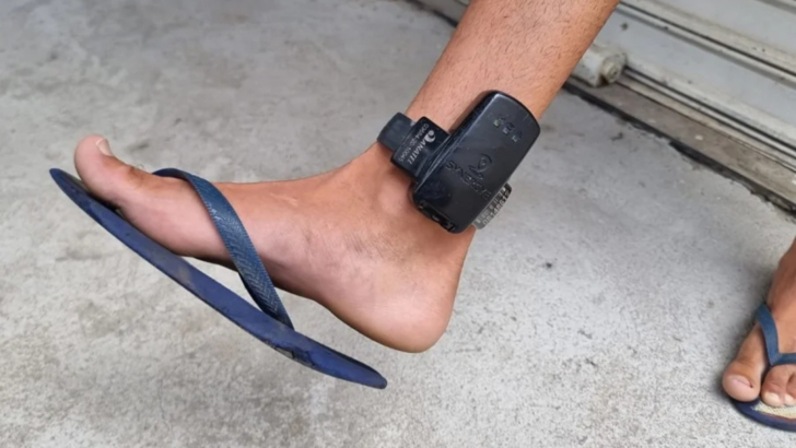 Pessoa usando tornozeleira eletrônica presa ao tornozelo e chinelo azul