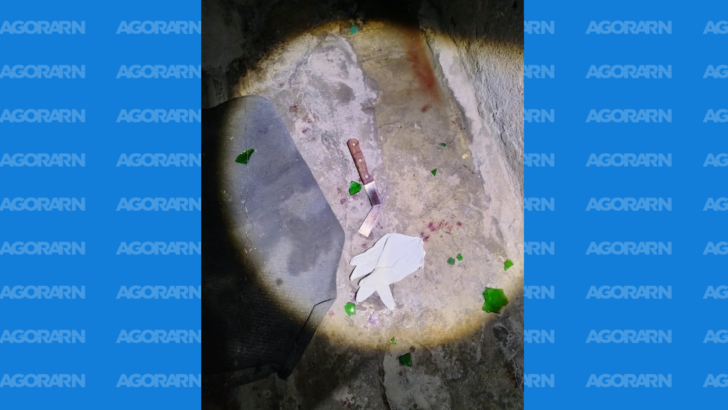 Faca no chão ao lado de uma luva branca e fragmentos de vidro em área iluminada -