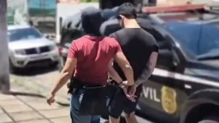 Agente conduz homem algemado em direção a veículo da Polícia Civil durante operação policial
