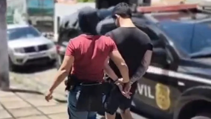 Agente conduz homem algemado em direção a veículo da Polícia Civil durante operação policial
