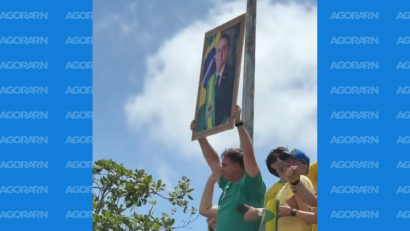 Homem ergue retrato de Jair Bolsonaro durante ato político ao ar livre
