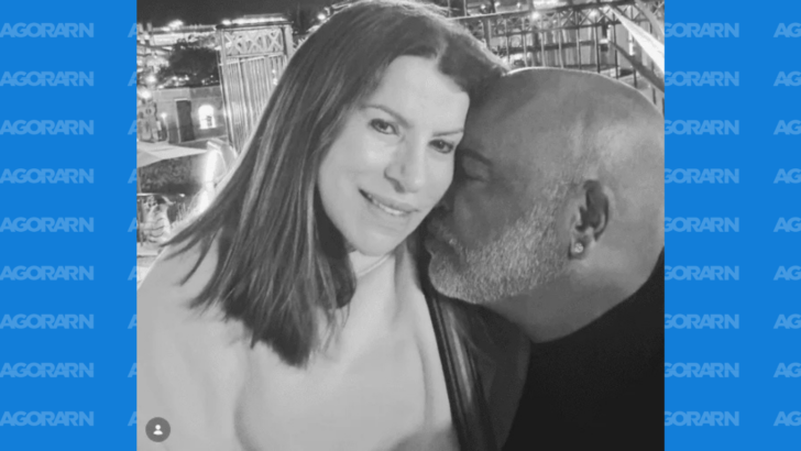 Registro em preto e branco mostra uma mulher ao lado de um homem, que aparece beijando seu rosto