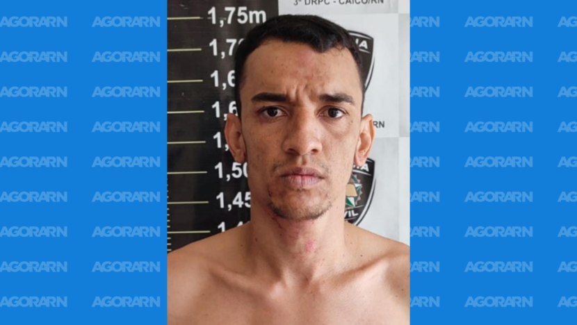 Homem fotografado diante de painel de identificação em uma unidade policial