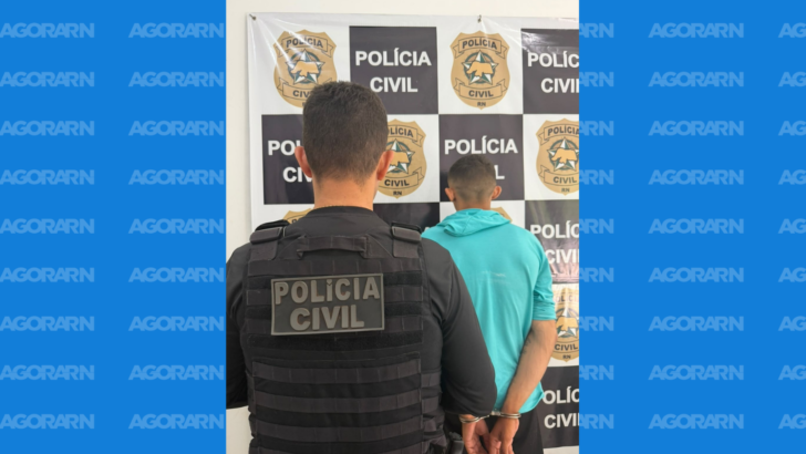 Policial civil aparece ao lado de homem algemado e de costas diante de painel da Polícia Civil do Rio Grande do Norte
