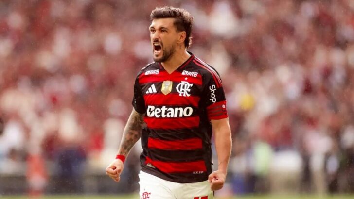 Jogador de futebol com uniforme rubro-negro comemora durante partida em estádio