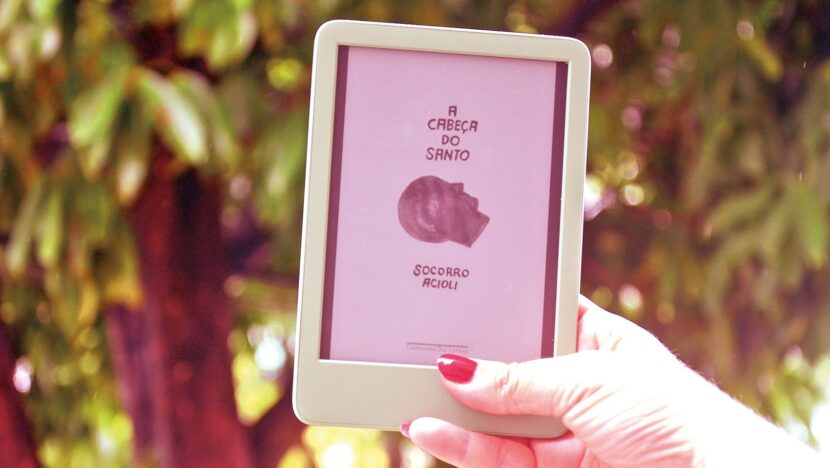 Mão segura leitor digital com a capa de um livro na tela, ao ar livre