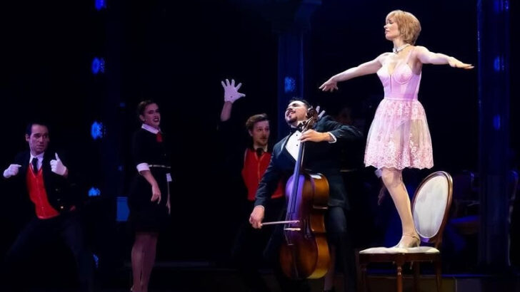 Cena do musical sobre Diana, com atriz sobre uma cadeira e músicos ao redor no palco