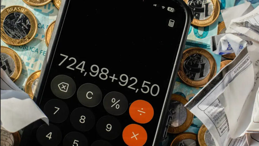 Calculadora aberta na tela de um celular sobre moedas, notas de real e cupons fiscais
