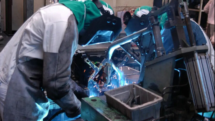 Trabalhador solda peças em linha de produção industrial