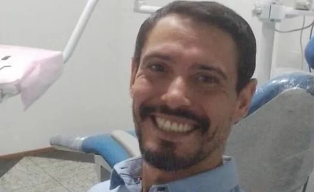 Homem sorrindo para a câmera enquanto está sentado em uma cadeira de atendimento odontológico