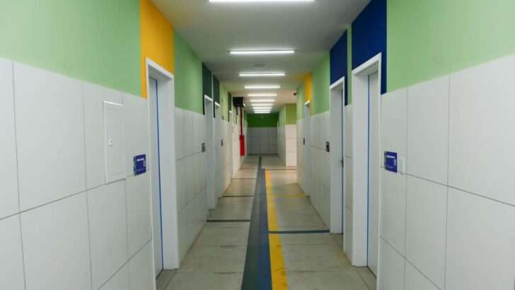 Corredor do hospital com portas, paredes verdes e faixas de orientação no piso