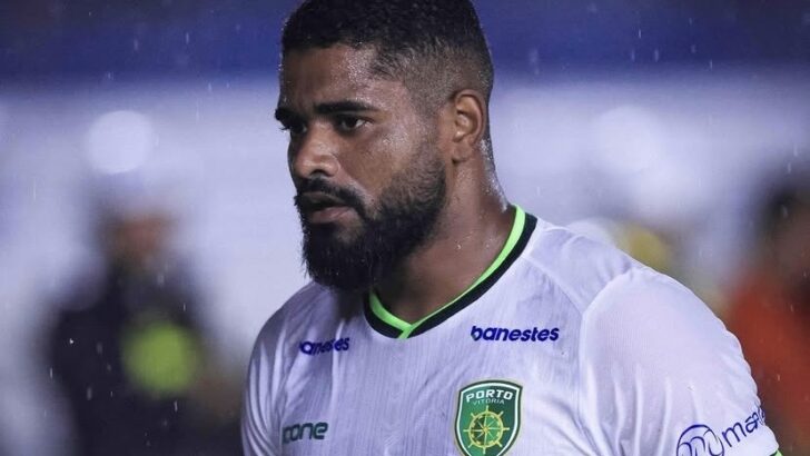 Jogador com uniforme branco do Porto Vitória aparece em campo durante uma partida de futebol