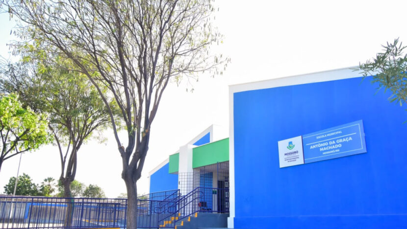Fachada azul e verde da escola, com rampa e corrimãos na entrada