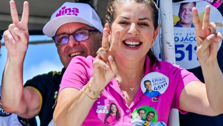 Nina Souza fala ao microfone durante ato político, com apoiadores ao fundo