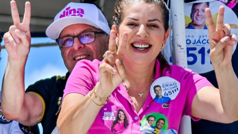 Nina Souza fala ao microfone durante ato político, com apoiadores ao fundo