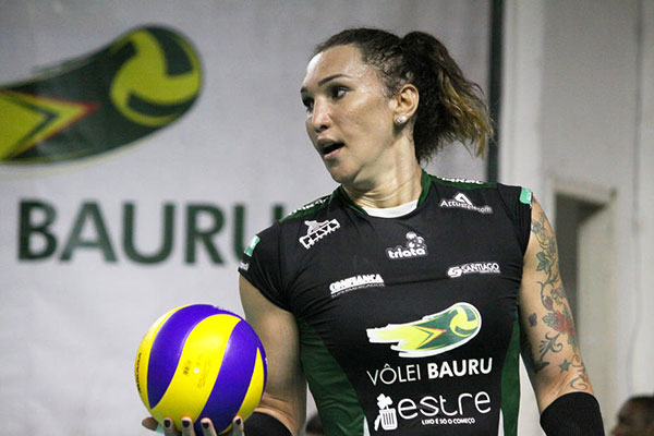Jogadora de vôlei com uniforme preto e verde do Vôlei Bauru segura uma bola amarela e roxa durante uma atividade esportiva