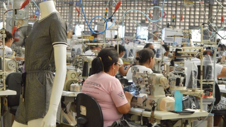 Trabalhadoras operam máquinas de costura em fábrica de roupas