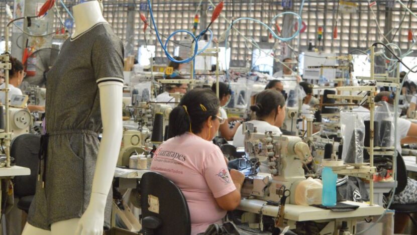 Trabalhadoras operam máquinas de costura em fábrica de roupas