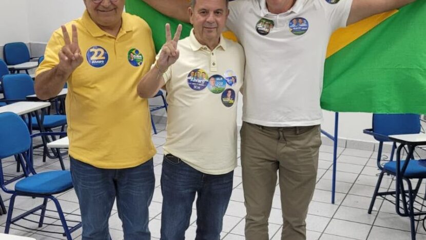 Três homens com camisetas de campanha posam diante de uma bandeira do Brasil