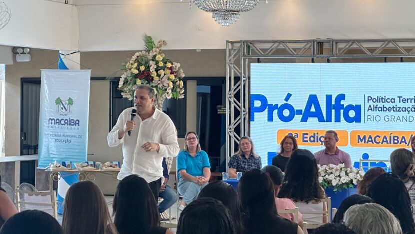 Palestrante fala ao microfone diante de educadores sentados em seminário de alfabetização