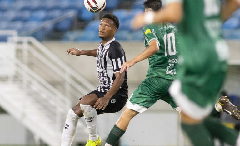 Jogador do ABC com uniforme preto e branco disputa lance com adversário de uniforme verde, enquanto a bola está no ar
