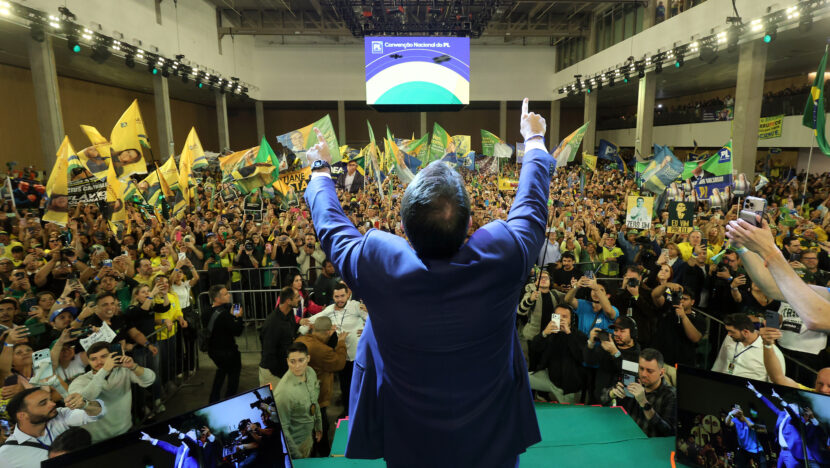 Flávio Bolsonaro, de costas no palco, ergue os braços diante do público na convenção nacional do PL