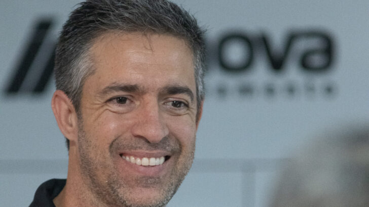Técnico João Burse sorri durante apresentação ao ABC, diante de painel com marcas dos patrocinadores