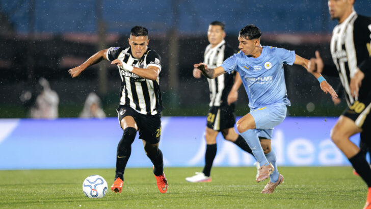 Jogador do Atlético-MG conduz a bola com atleta do City Torque ao lado, sob chuva