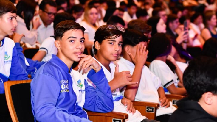Estudantes com uniforme da rede municipal sentados em auditório durante premiação